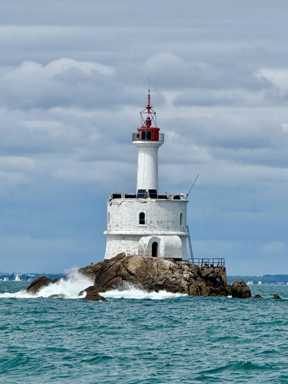 Weißer Leuchtturm mit rotem Dach über türkisfarbenem Meer.